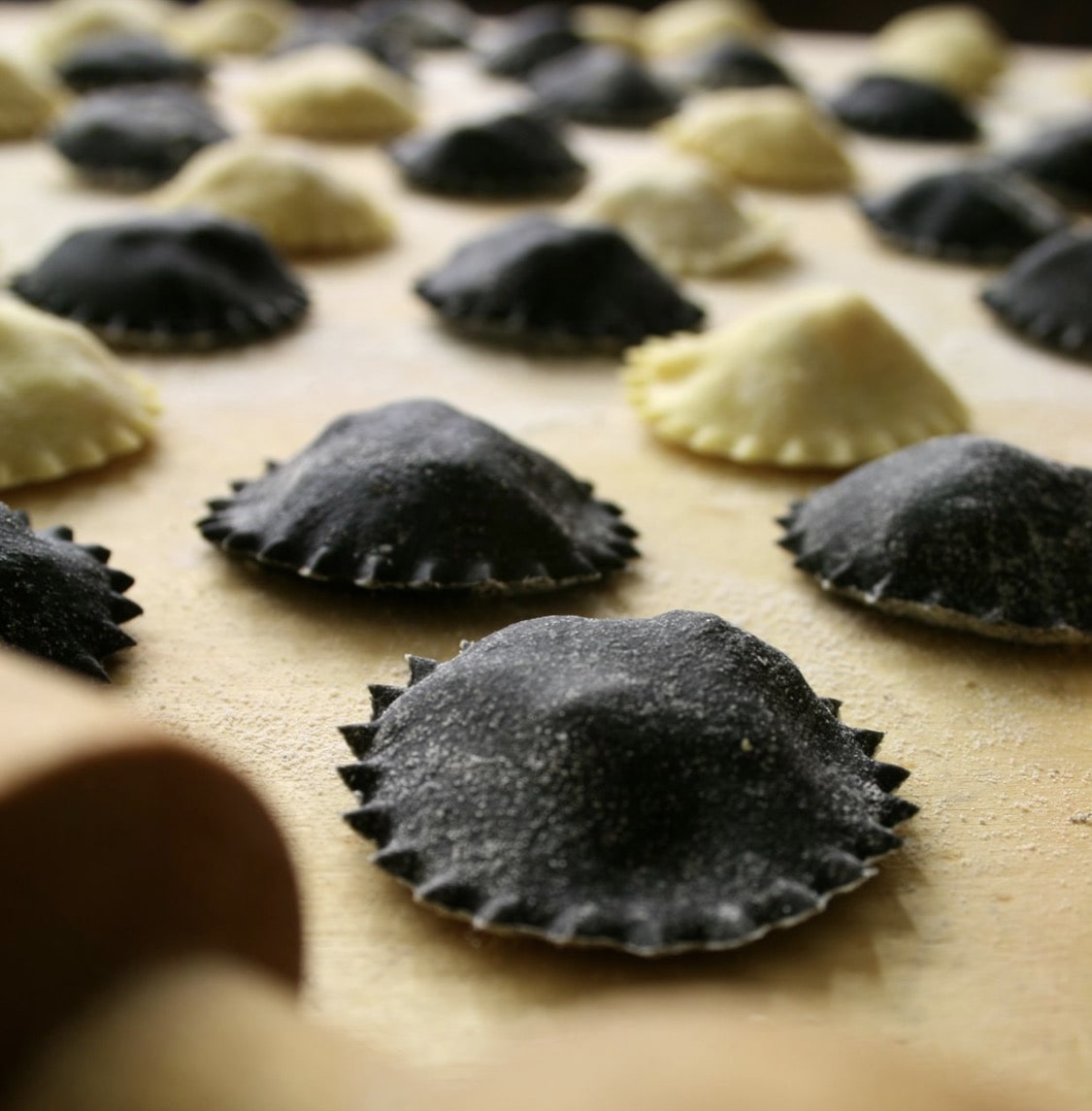 Close-up of black and pale stuffed pasta pieces arranged on a work surface with shallow depth of field.