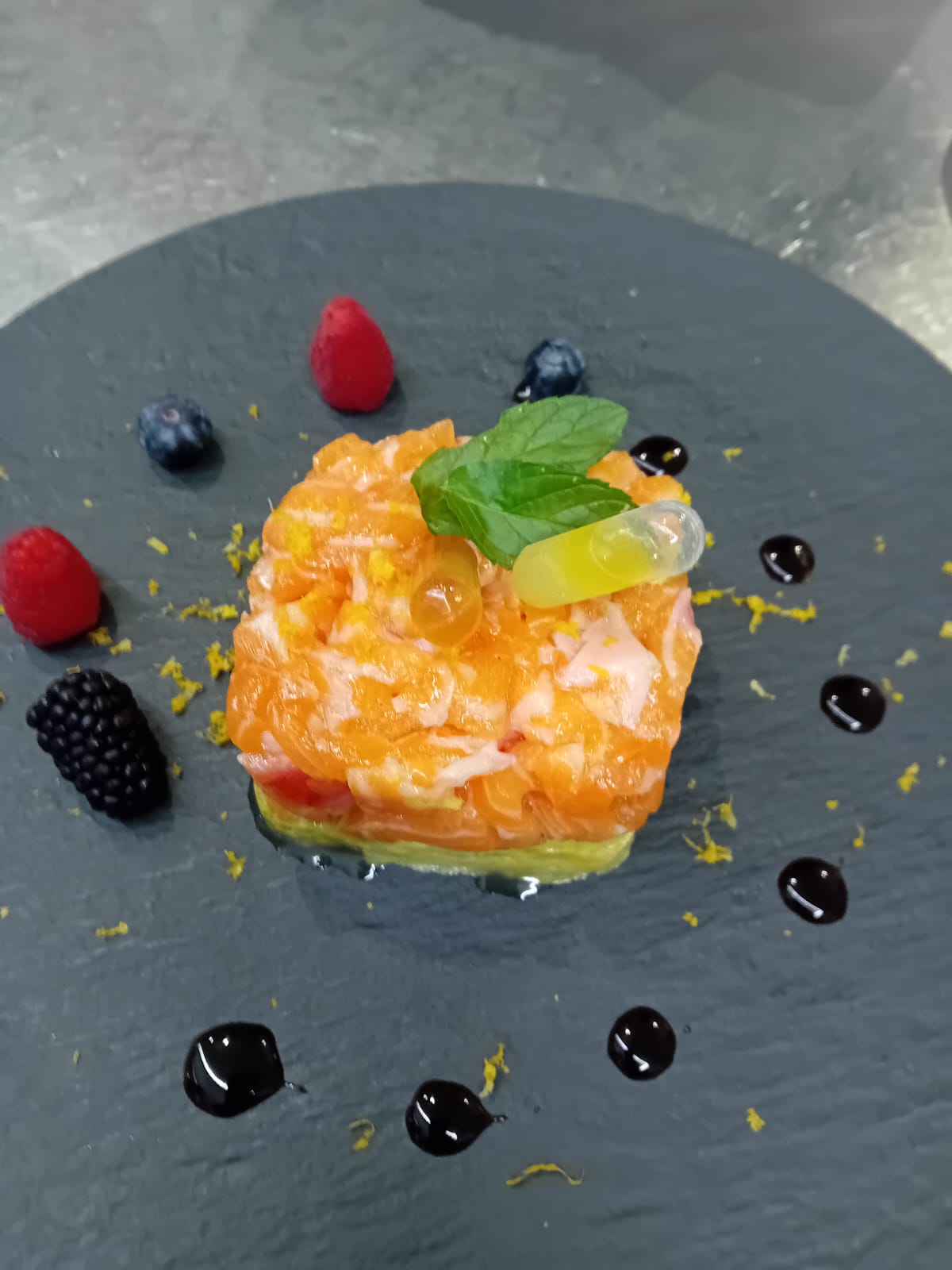 A square orange-topped plated dish with mint and berries on a dark slate plate, evenly lit.