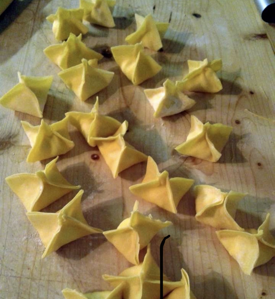 Overhead view of several uncooked folded pasta pieces scattered across a wooden cutting board.