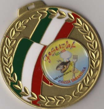 Close-up photograph of a round gold-toned medal with laurel decoration, green-white-red bands, and a central illustrated emblem, evenly lit.