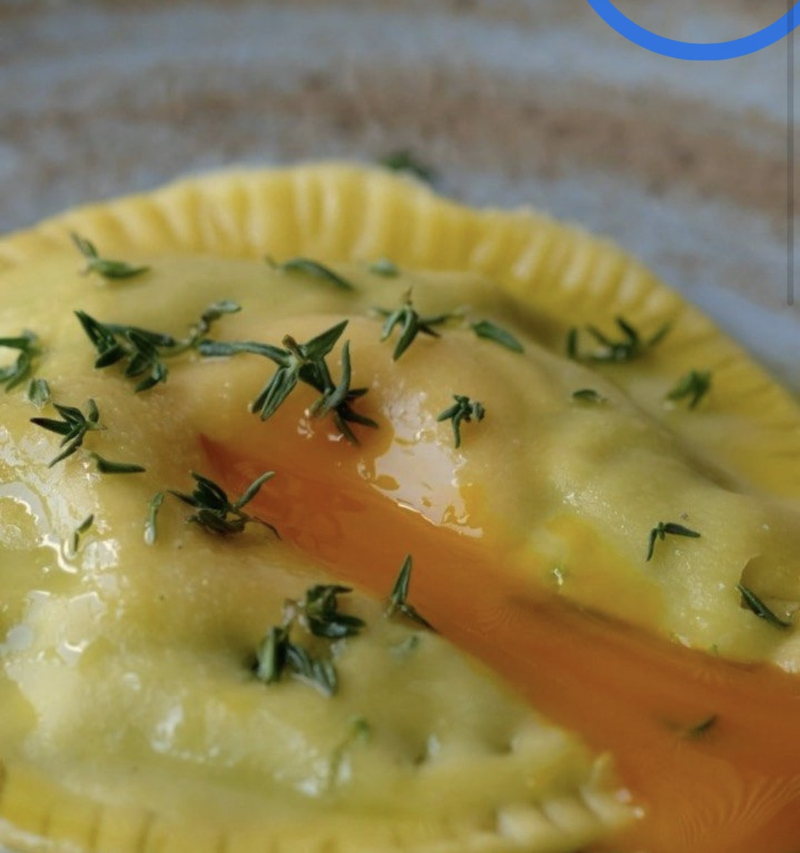 Close-up of a single stuffed pasta piece topped with herbs and oil, brightly lit.