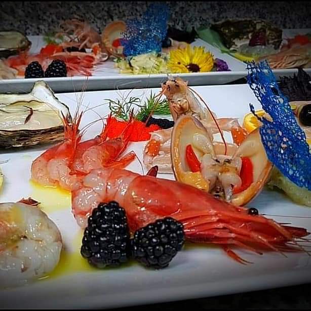 Close-up of a seafood platter with prawns, shellfish, berries and garnishes on white plates, dimly lit.